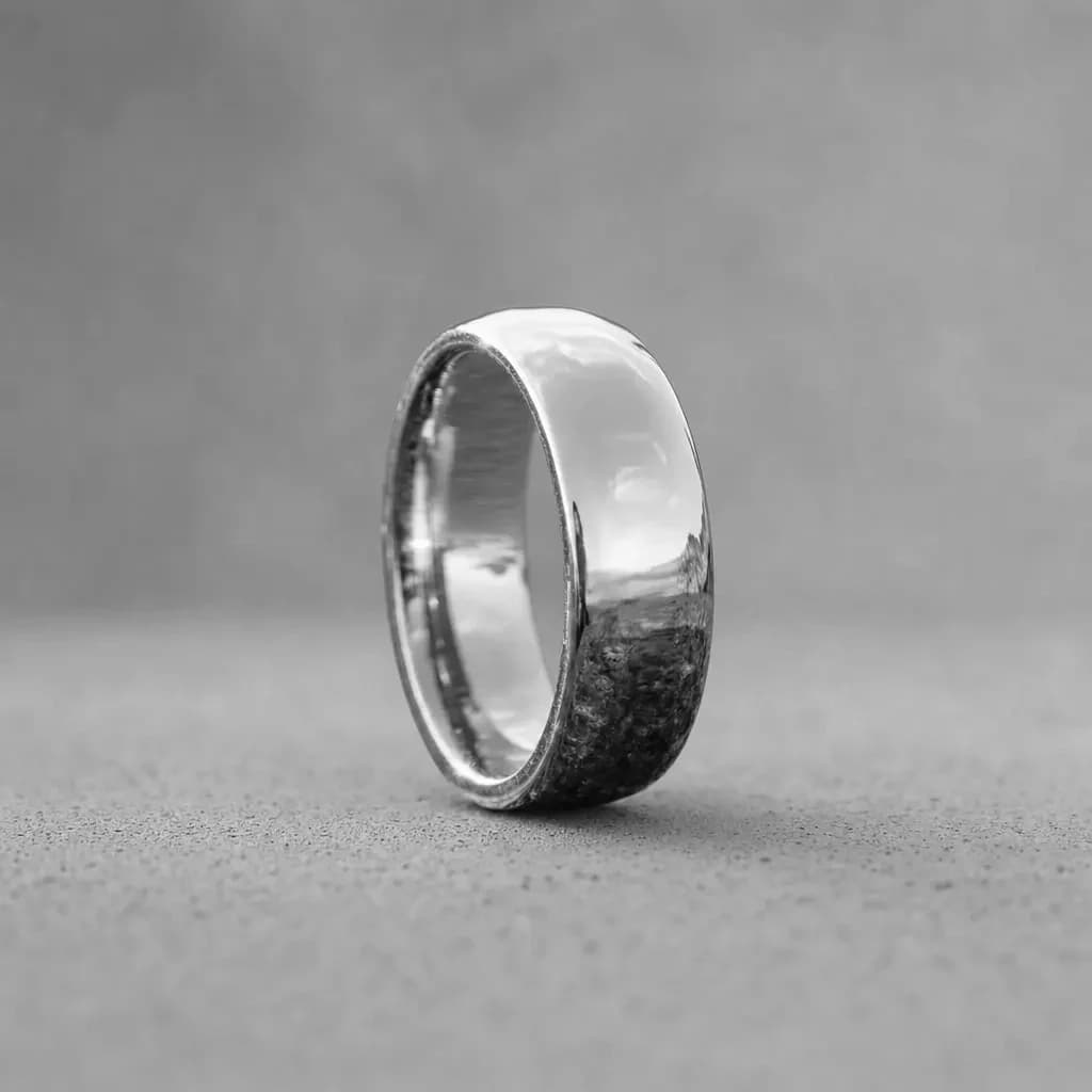 The Halo, an 8mm polished silver tungsten carbide band, standing upright on a poured concrete ledge